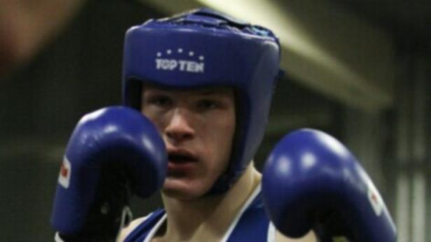 Ein junger Boxer mit blauem Kopfschutz und Boxhandschuhen.