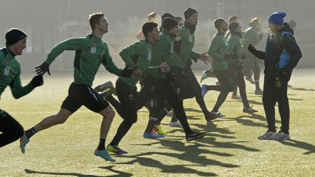 Eine Gruppe von Fußballspielern läuft während des Trainings auf dem Platz, während der Trainer zusieht.