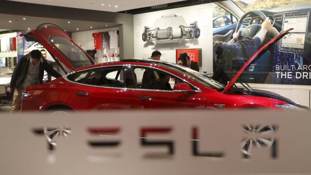 Ein rotes Tesla-Auto steht in einem Ausstellungsraum mit geöffneter Motorhaube und Kofferraum.