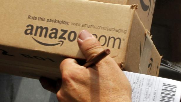 Eine Hand hält einen Amazon-Karton mit der Aufschrift „Rate this packaging: www.amazon.com/packaging“.