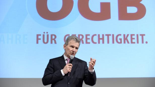 Ein Mann in Anzug und Krawatte spricht vor einem Hintergrund mit der Aufschrift „70 Jahre für Gerechtigkeit“.