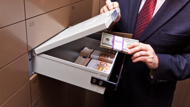 Ein Mann öffnet ein Bankschließfach gefüllt mit Bündeln von Euro- und Dollar-Scheinen.