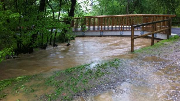 Ein überfluteter Fluss unterspült eine kleine Holzbrücke.