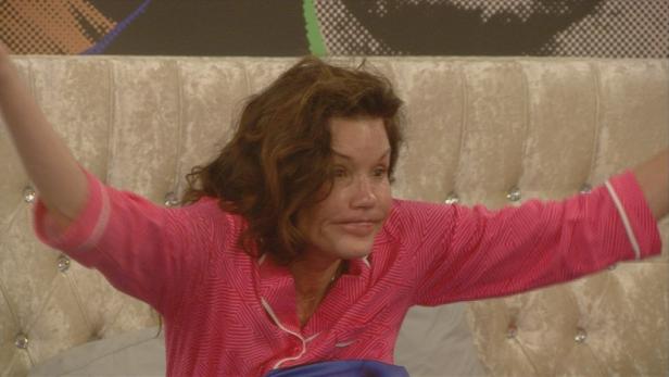 Eine Frau im pinkfarbenen Pyjama liegt mit erhobenen Armen im Bett.