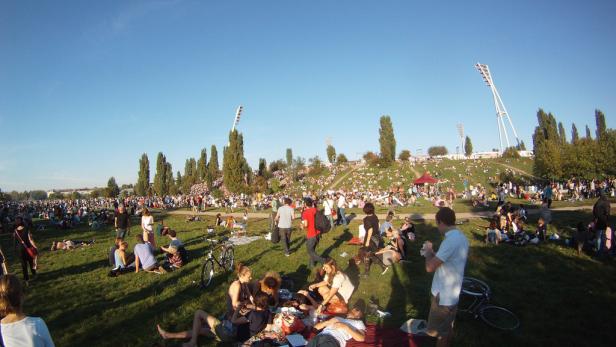 Viele Menschen entspannen sich an einem sonnigen Tag im Park auf einer Wiese.