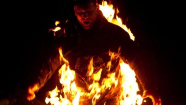 Eine Person steht inmitten von Flammen und schreit.