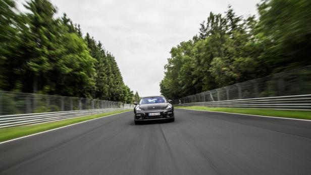 Ein schwarzer Porsche fährt auf einer Rennstrecke mit Bäumen im Hintergrund.