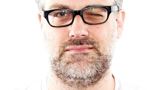 Ein Mann mit Brille zwinkert in die Kamera.