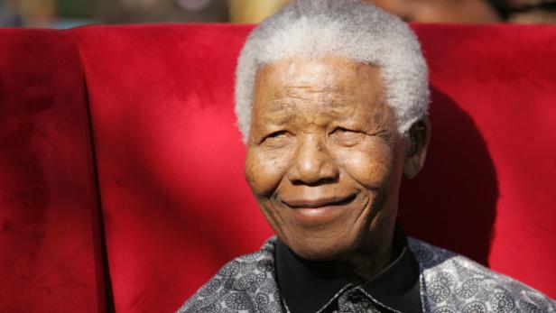 Nelson Mandela lächelt vor einem roten Hintergrund.