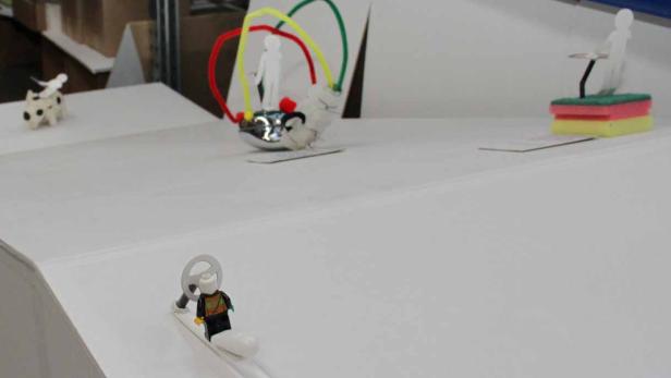 Eine surreale Szene mit verschiedenen kleinen Figuren und Objekten auf einer weißen Oberfläche.