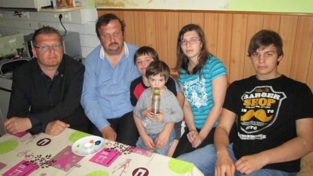 Eine Familie sitzt an einem Tisch mit einer gemusterten Tischdecke.