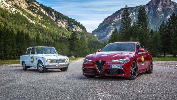 Zwei Alfa Romeo Autos, ein Oldtimer und ein modernes Modell, vor einer Bergkulisse.