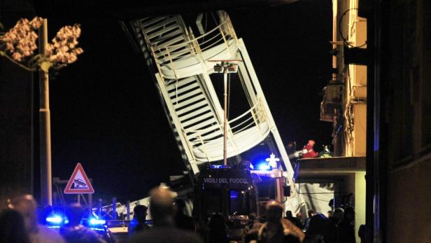 Ein Feuerwehrwagen mit ausgefahrener Leiter steht nachts vor einem Gebäude in Genua.