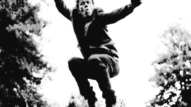Ein Mann in Anzug und Hut springt in der Luft, die Faust geballt.