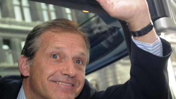 Ein Mann im Anzug winkt aus einem Auto.