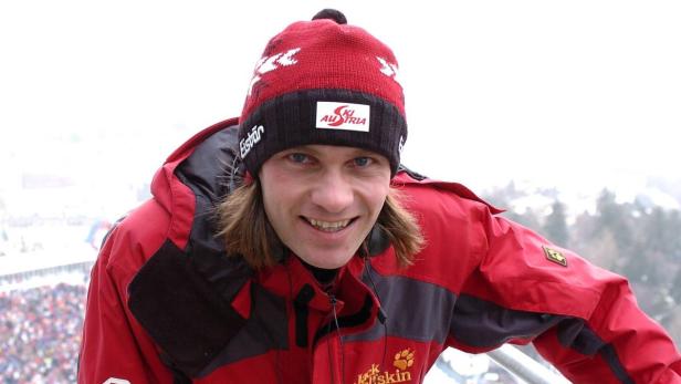 Andreas Goldberger mit roter Jacke und Mütze vor einer Zuschauermenge.