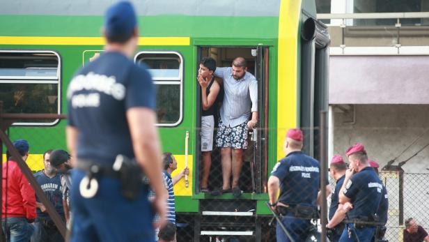 Zwei Männer stehen in der Tür eines grünen Zuges, bewacht von Polizisten.