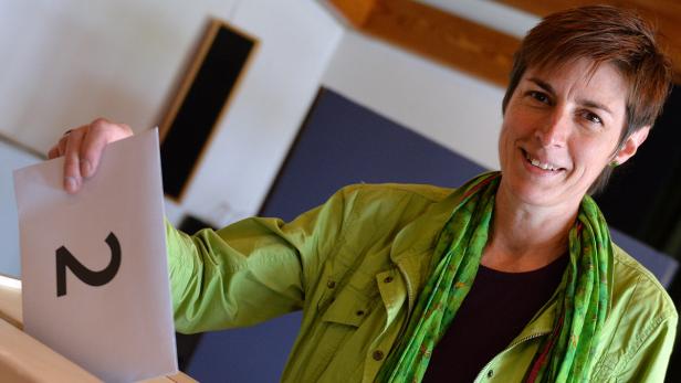 Eine Frau wirft einen Stimmzettel mit der Zahl 2 in eine Wahlurne.