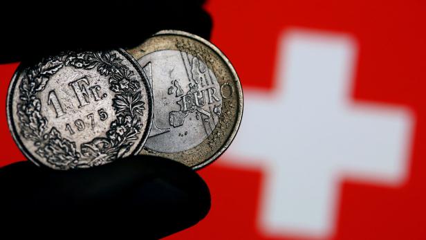 Eine Schweizer Franken-Münze und eine Euro-Münze vor der Schweizer Flagge.