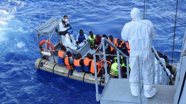 Ein Schlauchboot mit Menschen in Rettungswesten wird von Helfern in Schutzanzügen betreut.