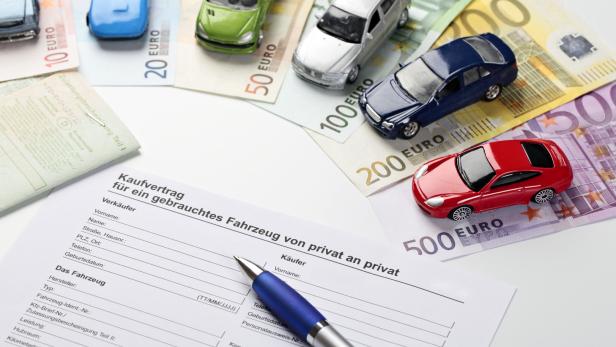 Ein Kaufvertrag für ein gebrauchtes Fahrzeug liegt neben Spielzeugautos und Euro-Banknoten.
