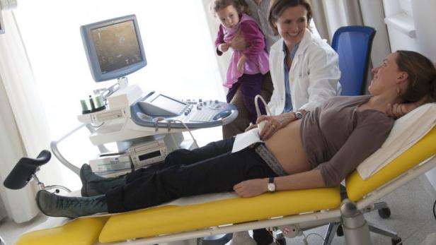 Eine schwangere Frau liegt auf einer Liege, während eine Ärztin einen Ultraschall durchführt.