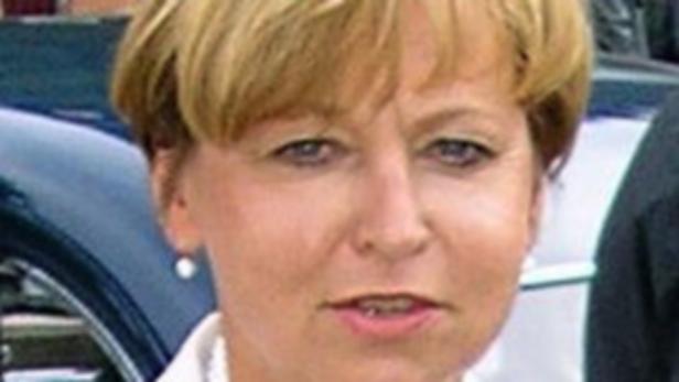 Porträt einer Frau mit blonden, kurzen Haaren vor einem blauen Auto.
