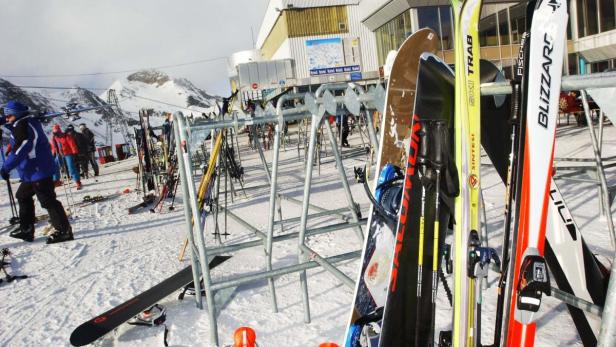 Skier und Snowboards stehen an einer Skistation im Schnee.