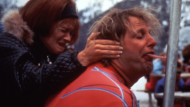 Eine weinende Frau hält den Kopf eines Mannes fest, der seine Zunge an eine Metallstange hält.