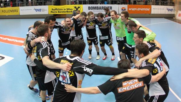 Eine Handballmannschaft umarmt sich im Kreis auf dem Spielfeld.