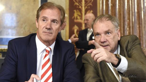 Zwei Männer in Anzügen sitzen an einem Tisch und diskutieren.