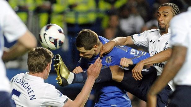 Ein Fußballspieler tritt nach dem Ball, während er von zwei Gegenspielern bedrängt wird.