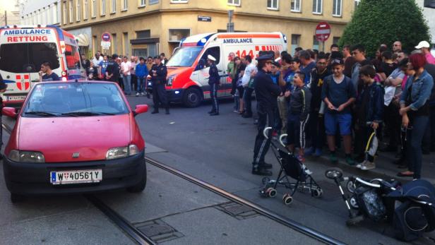 Ein rotes Auto steht auf einer Straße in Wien, umringt von Menschen und Rettungswagen.