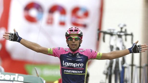 Ein Radrennfahrer in pinkfarbenem Trikot jubelt mit erhobenen Armen.