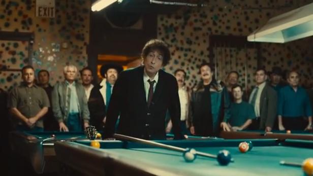 Bob Dylan steht an einem Billardtisch, umgeben von einer Gruppe Männer.