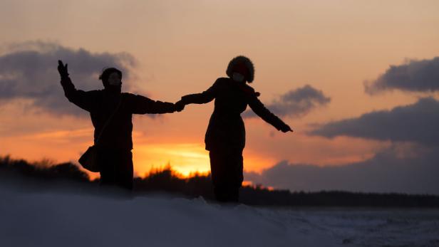 Zwei Personen halten Händchen im Sonnenuntergang.