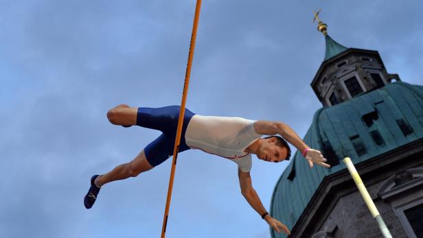 Ein Stabhochspringer überquert die Latte vor dem Hintergrund einer Kirche.