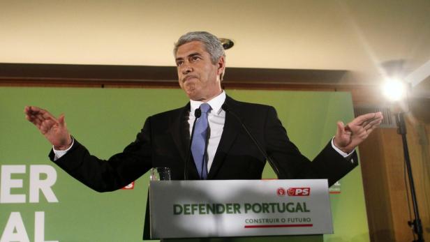 Ein Mann in einem Anzug gestikuliert hinter einem Rednerpult mit der Aufschrift „Defender Portugal“.