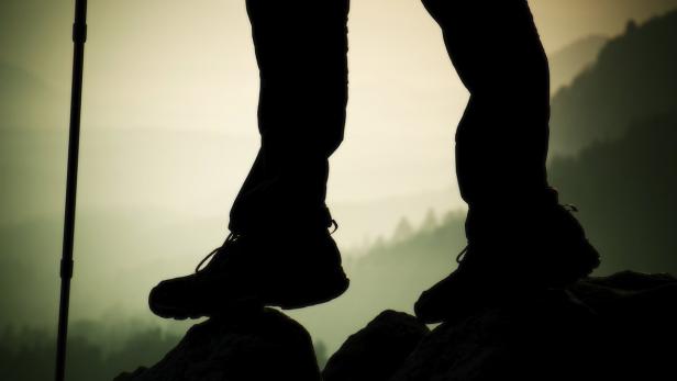 Die Füße eines Wanderers stehen auf einem Felsen in den Bergen.