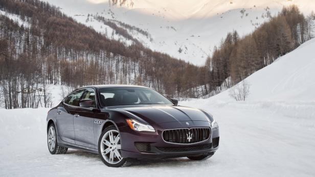Ein dunkelroter Maserati steht im Schnee vor einer Berglandschaft.
