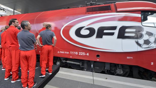 Eine Gruppe von Männern steht vor einer roten ÖBB-Lokomotive mit Fußball-Logo.