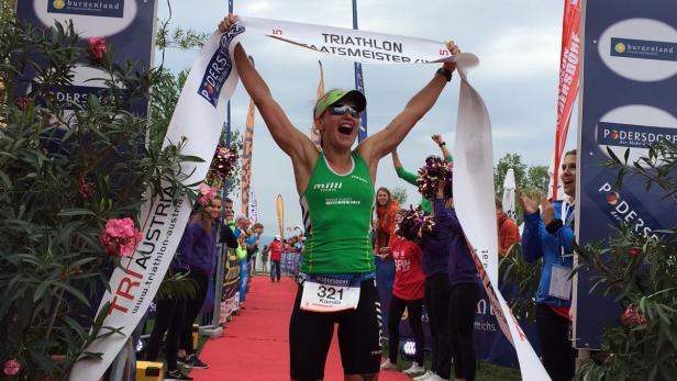 Eine Triathletin überquert die Ziellinie und reißt das Siegerband in die Höhe.