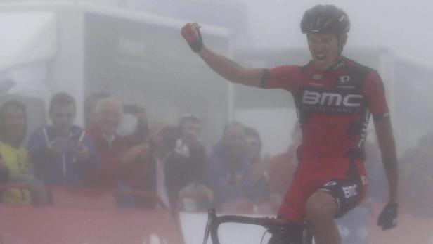 Ein Radrennfahrer jubelt mit erhobener Faust inmitten von Zuschauern im Nebel.