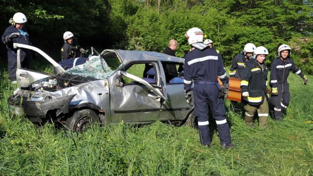 NIEDERÖSTERREICH: ZWEI TOTE BEI VERKEHRSUNFALL AUF Ein schwer beschädigtes Auto liegt im Gras, während Feuerwehrleute vor Ort sind.