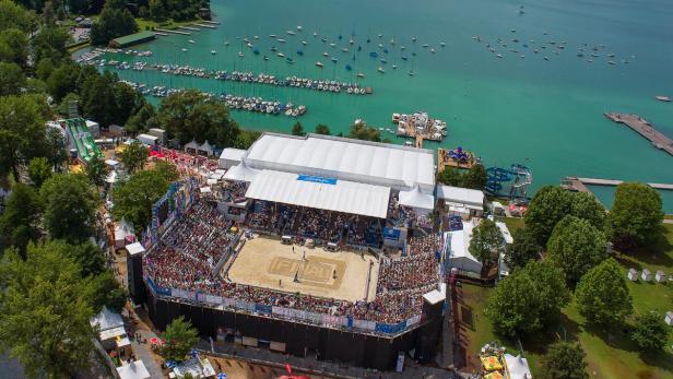 Ein vollbesetztes Beachvolleyballstadion am Ufer eines Sees mit vielen Segelbooten.