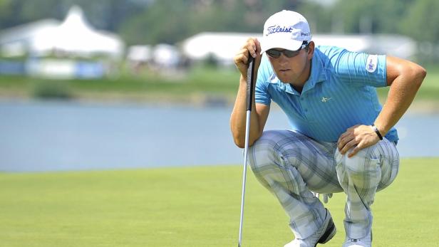 Ein Golfspieler kauert auf dem Grün und zielt mit seinem Putter.