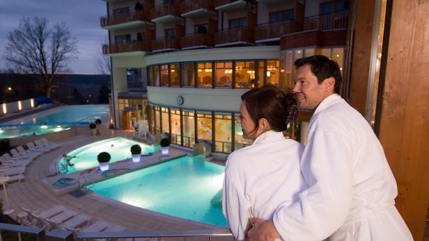 Ein Paar in Bademänteln blickt auf die beleuchteten Pools eines Resorts.