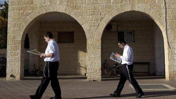 Zwei jüdische Männer gehen lesend unter Steinbögen entlang.