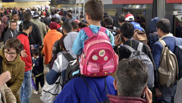 Ein Kind mit einem rosa Rucksack sitzt auf den Schultern einer Person in einer Menschenmenge.