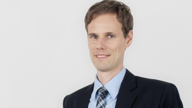 Ein lächelnder Mann im Anzug vor einem weißen Hintergrund.